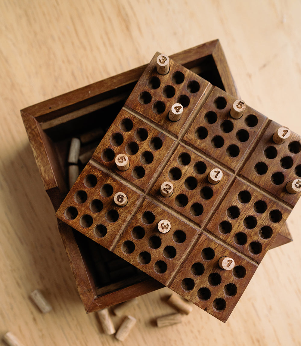 Wooden peg sudoku board with circular holes and small numbered wooden pieces
