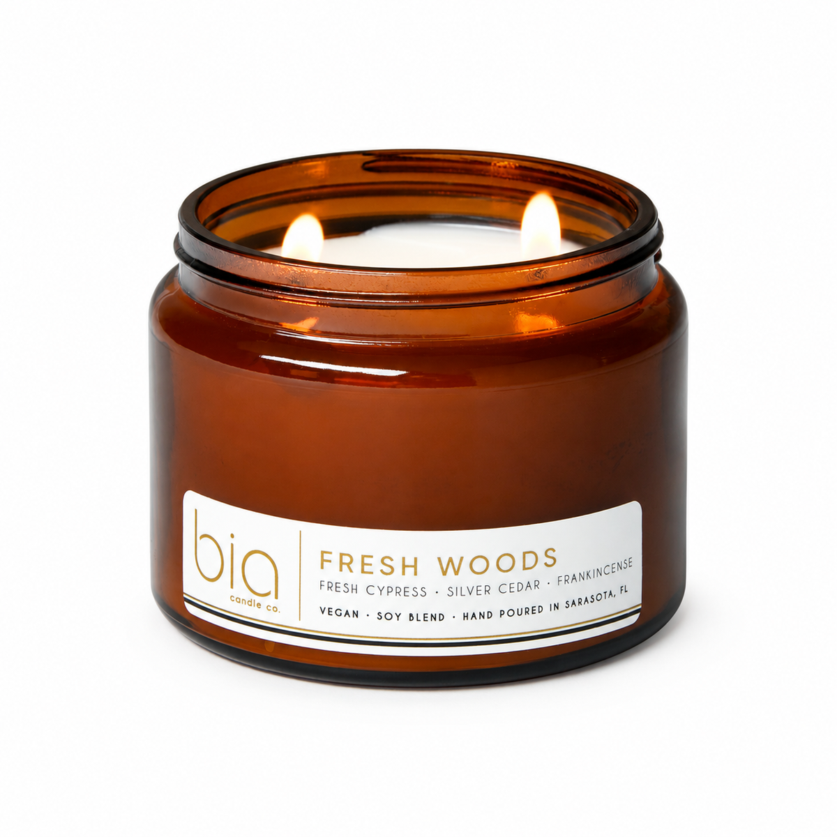 Amber glass soy blend candle jar with lit flame and Fresh Woods label