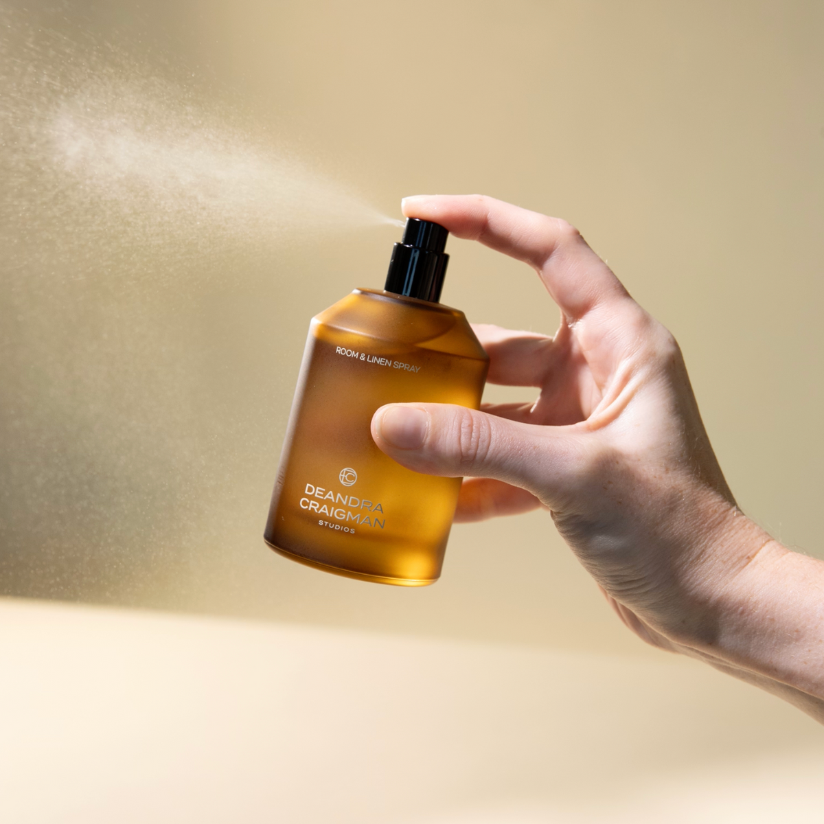 Amber room spray bottle with black cap being held for use