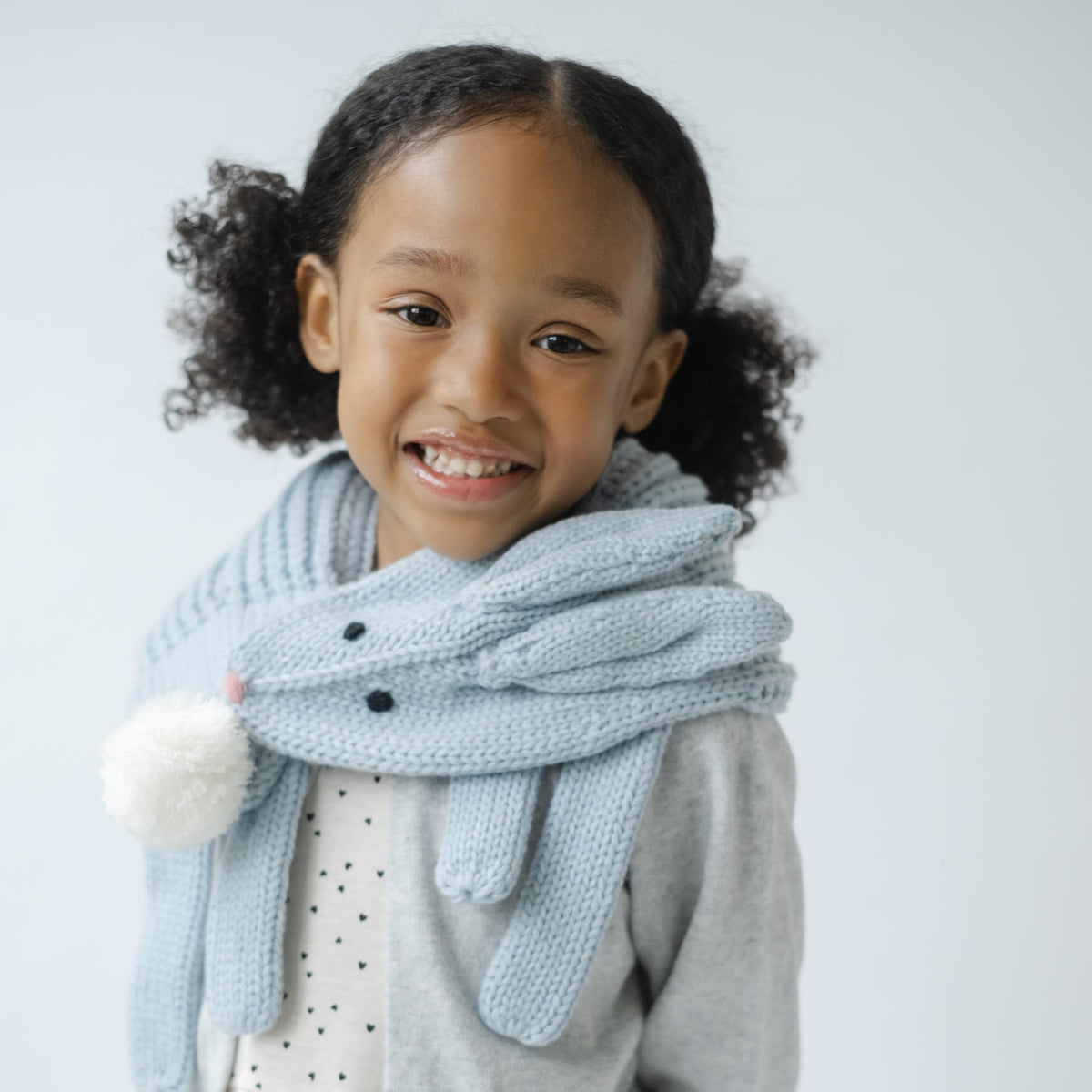 Pale blue rabbit scarf worn around a child's neck, with a pom-pom tail