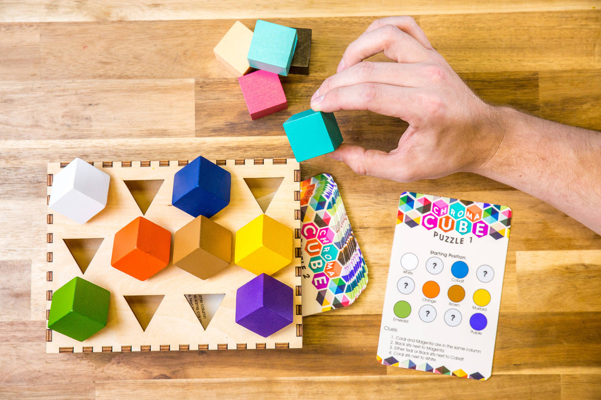 Hand placing multicolor cubes on wooden logic board with instruction booklet