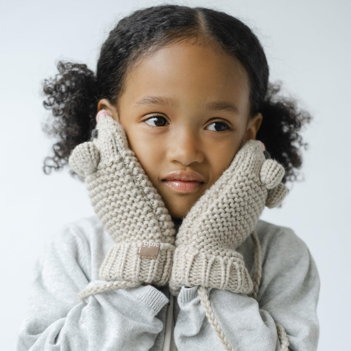 Oat beige mouse-face knit mittens with connecting cord, worn on a child’s hands