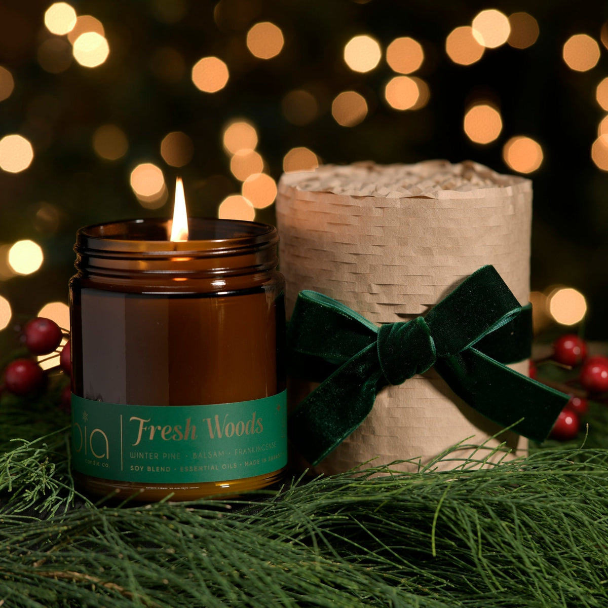Amber candle jar with lit wick, green label, and dark green holiday bow