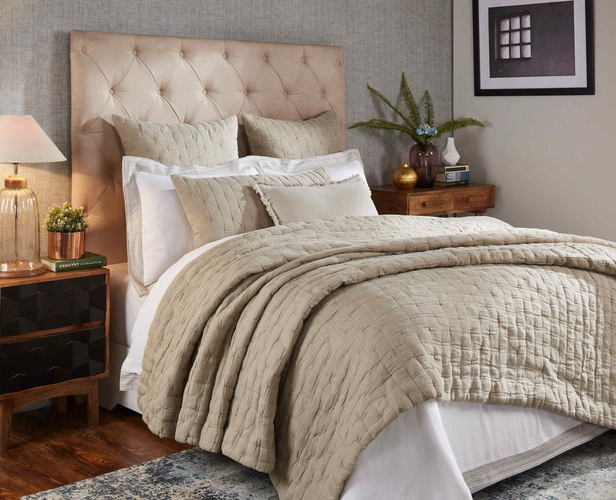 Light beige linen quilt on bed with quilted pinched texture and neat edges.