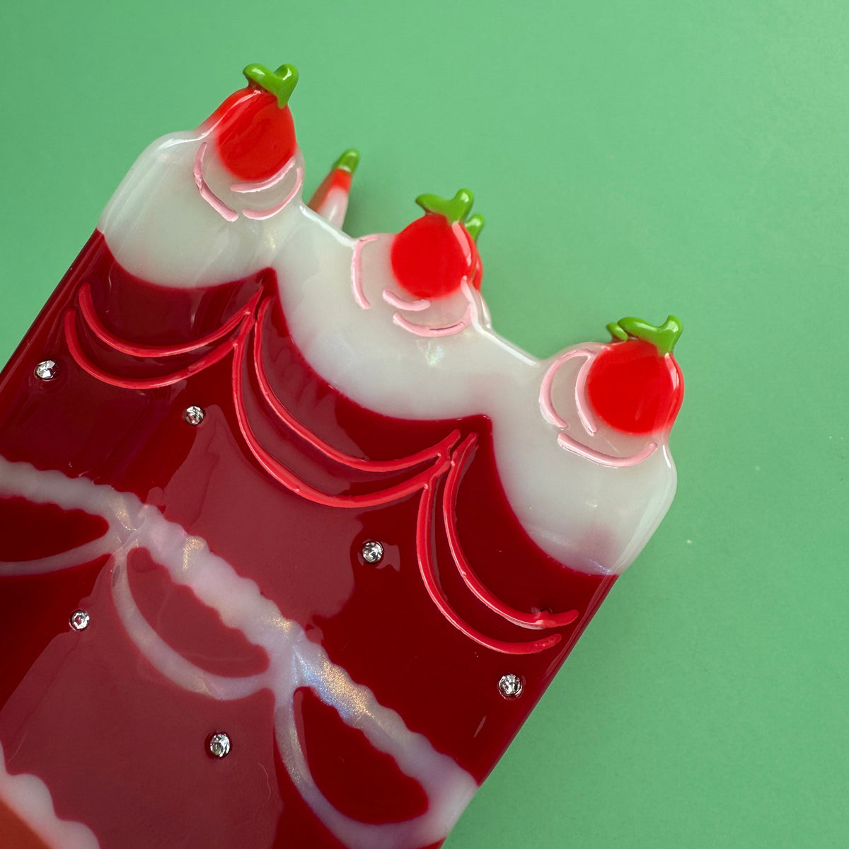 Cake hair claw close-up with red scalloped frosting lines and small rhinestone dots