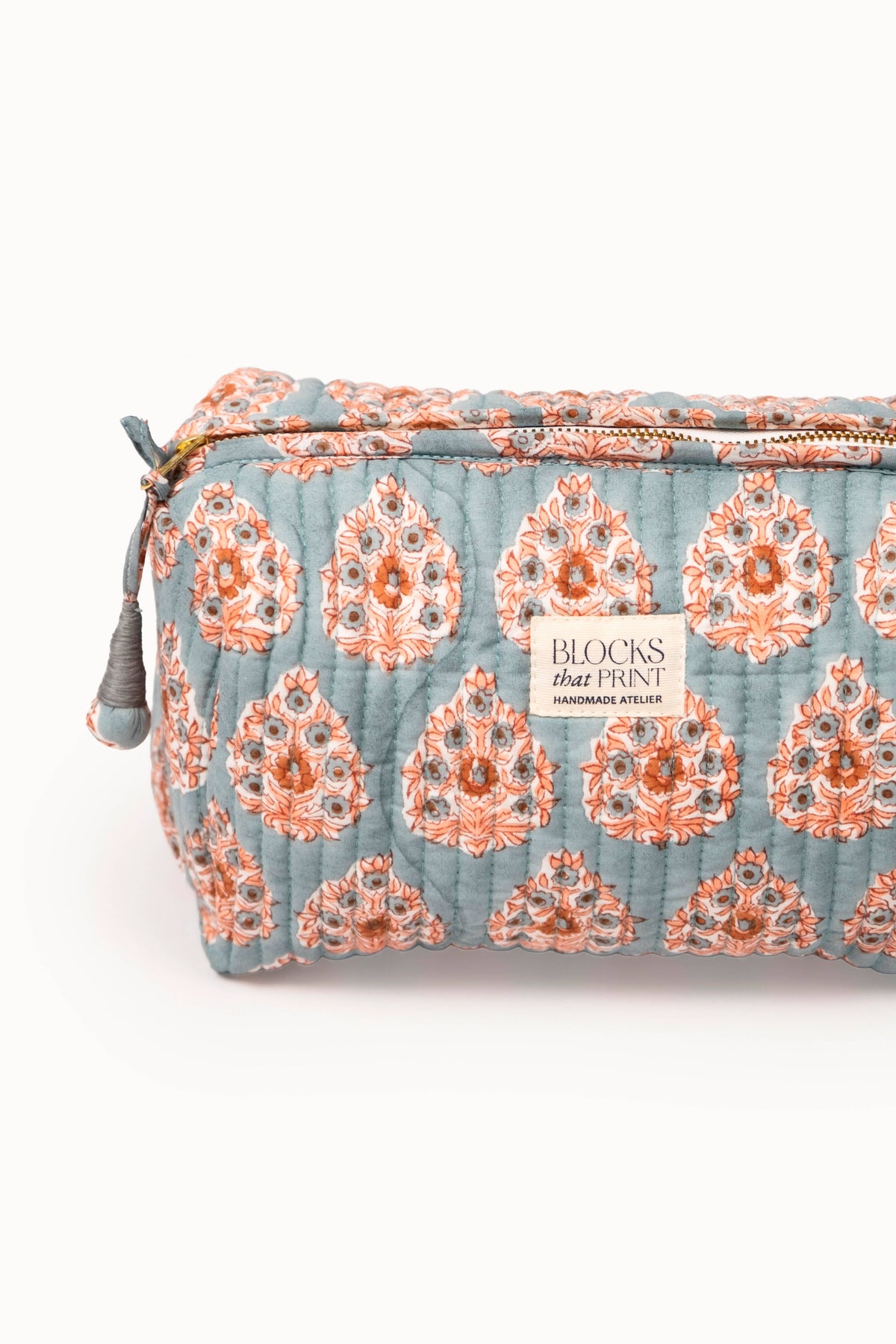 Quilted travel pouch close-up with terracotta buta block print, zipper edge, and label
