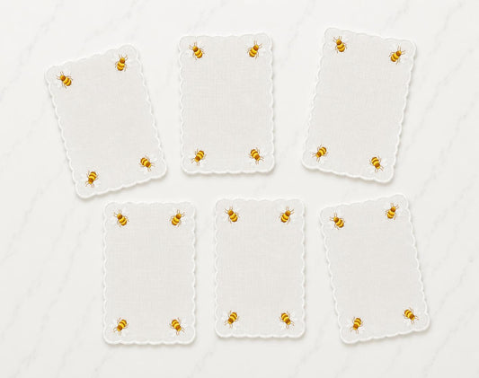 Six white cocktail napkins with scalloped edges, embroidered honey bees in corners