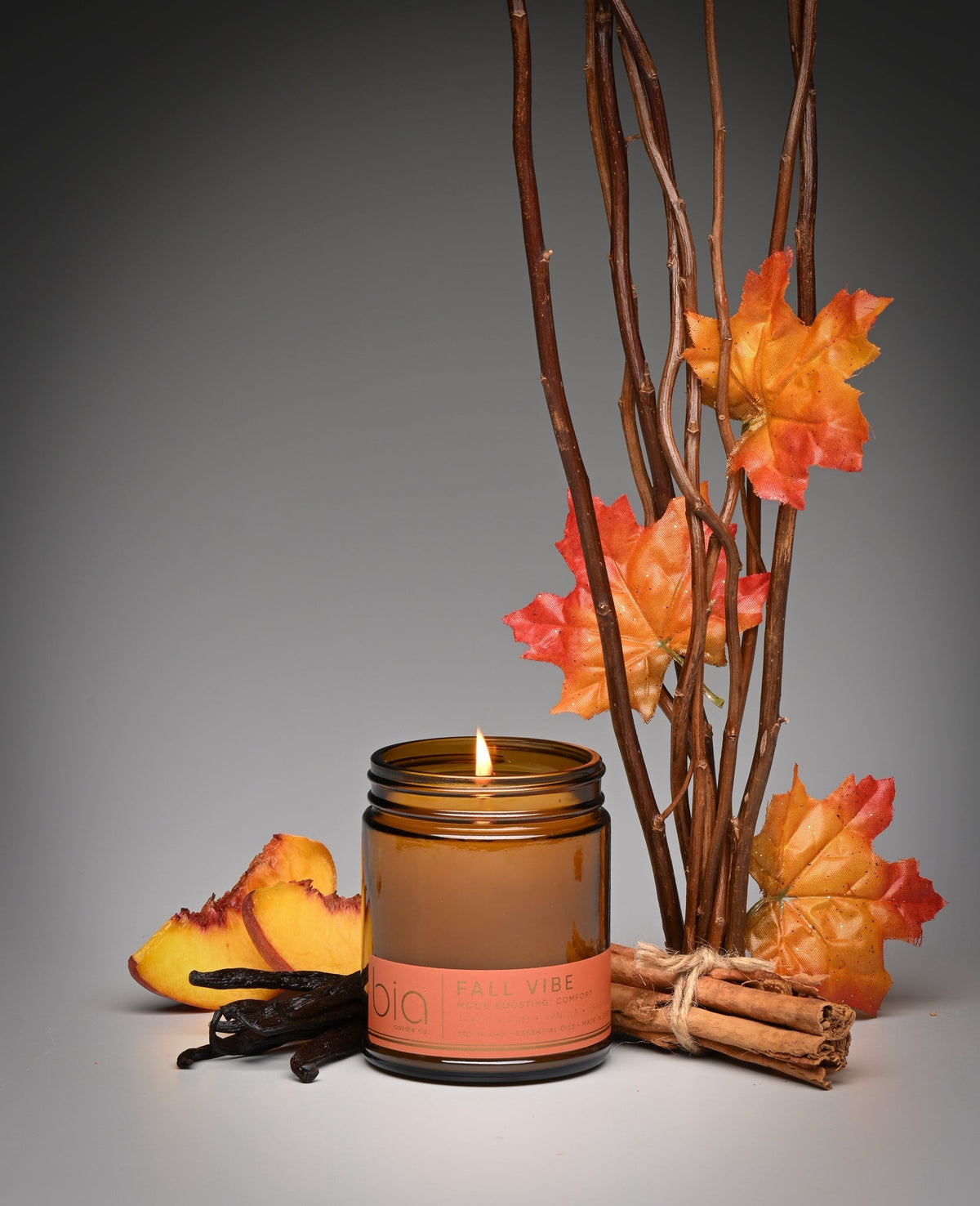 Lit amber soy candle jar on white surface with autumn leaves and twigs decor