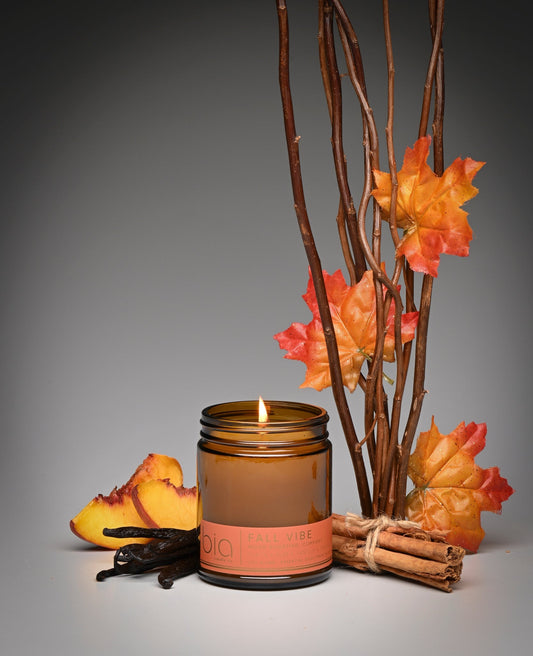 Lit amber soy candle jar on white surface with autumn leaves and twigs decor