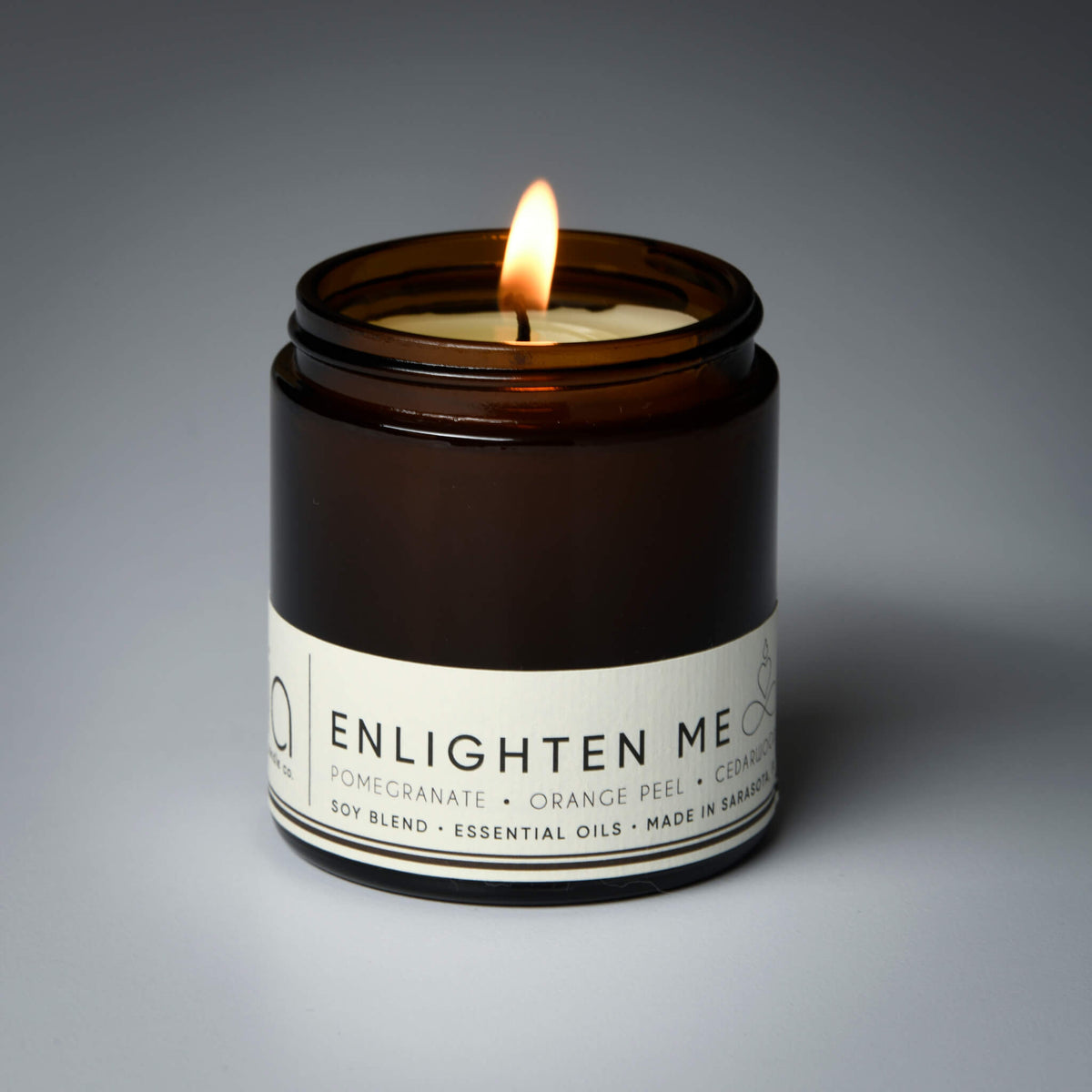 Lit soy blend candle in amber jar with ENLIGHTEN ME label facing camera