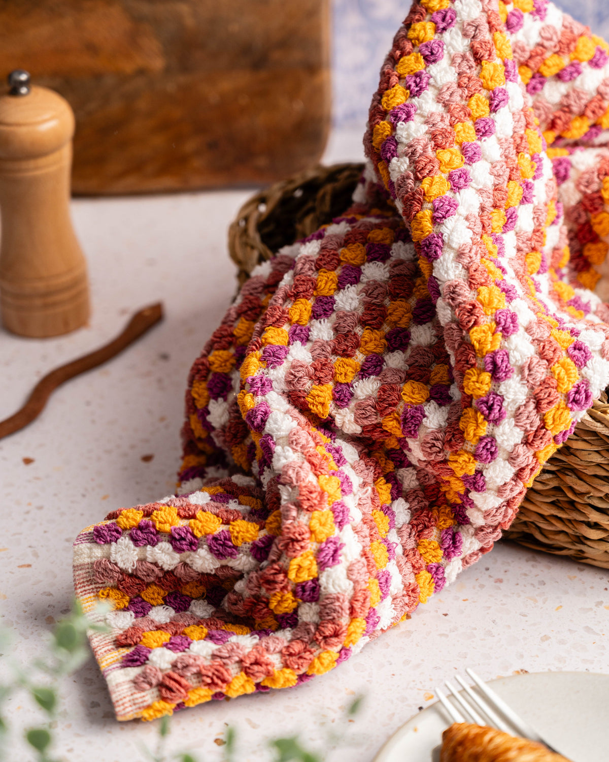 Close-up of folded checkered hand towel in orange, purple, and cream tones, no tassels.