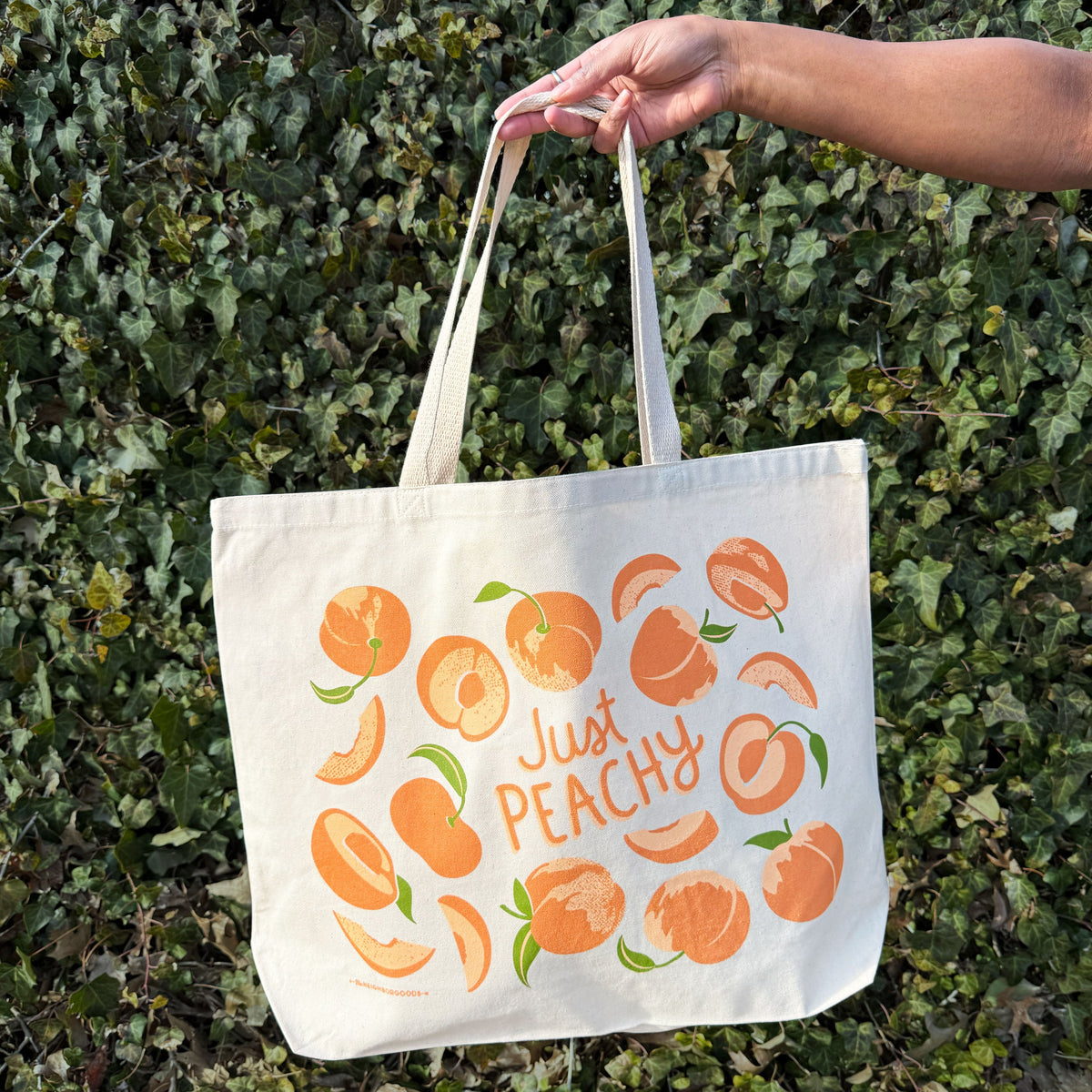 Peach print canvas tote bag held by hand, showing “Just Peachy” front design