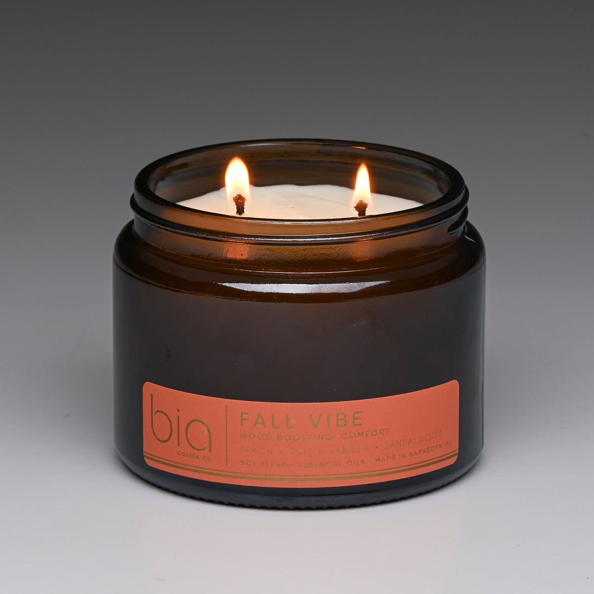 Amber glass candle jar with two flames, orange label on front