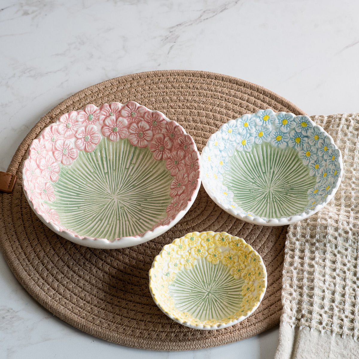 Embossed daisy ceramic bowls on placemat: pink and blue plus a small yellow bowl