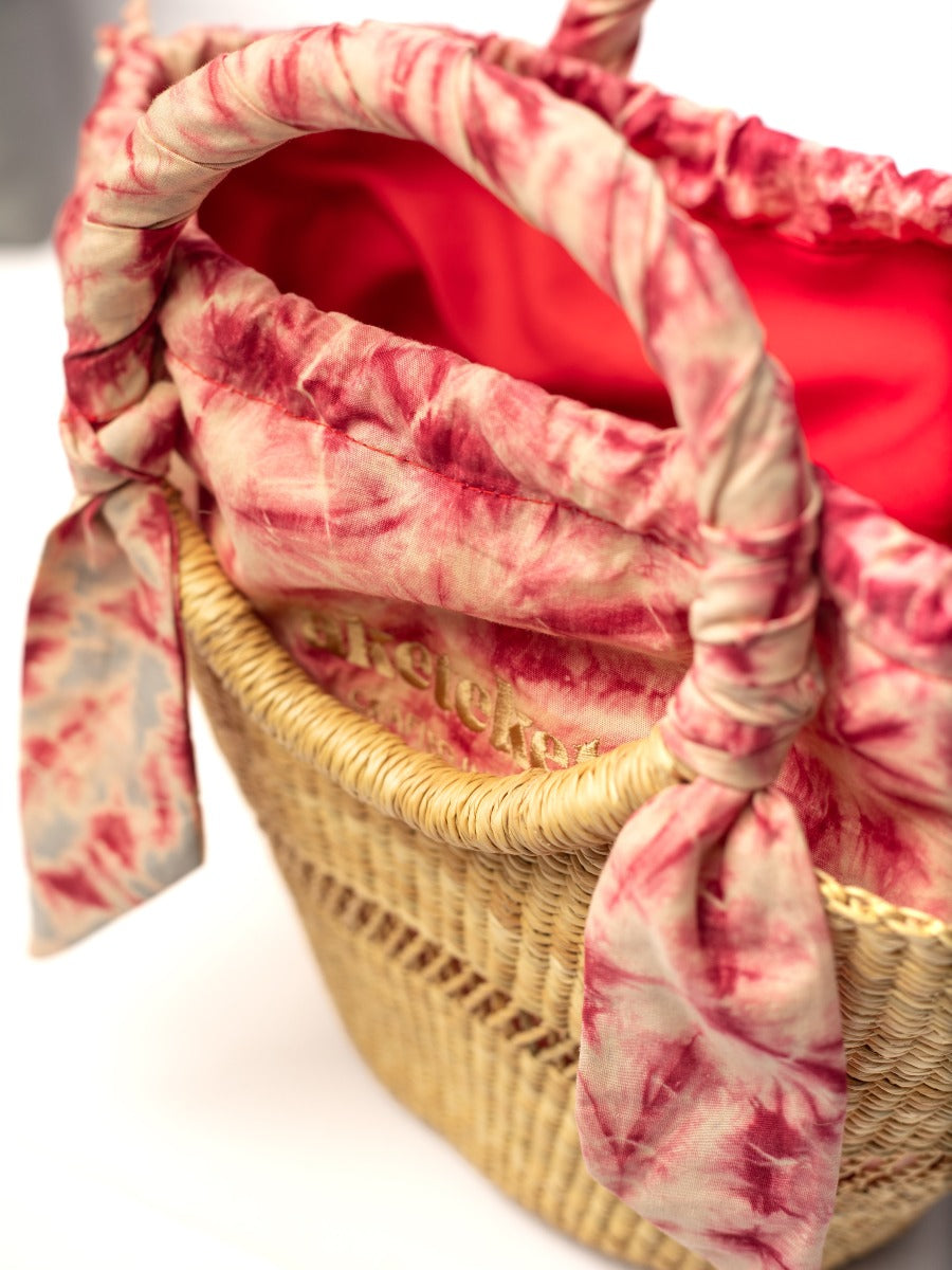 Small woven straw bag close-up with red lining and red tie-dye handle wrap