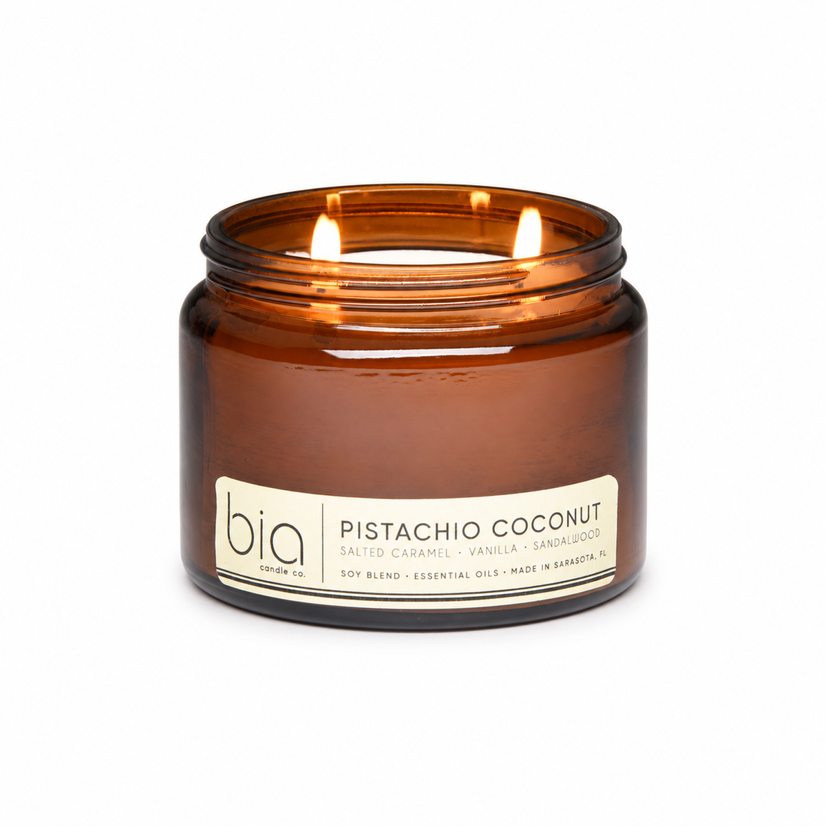 Amber glass candle jar with lit wick and Pistachio Coconut label on front.