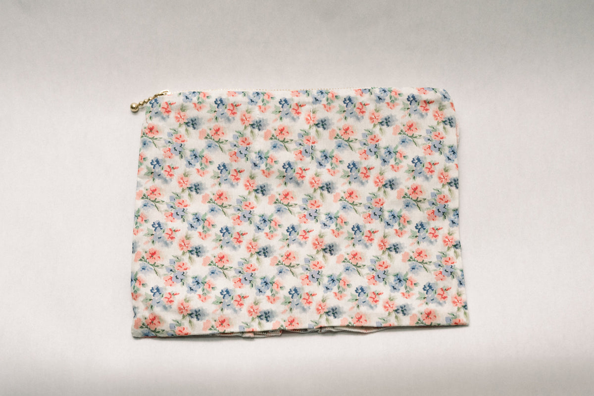 Floral zipper pouch with ruffled front hem and light blue floral print, gold zipper pull detail