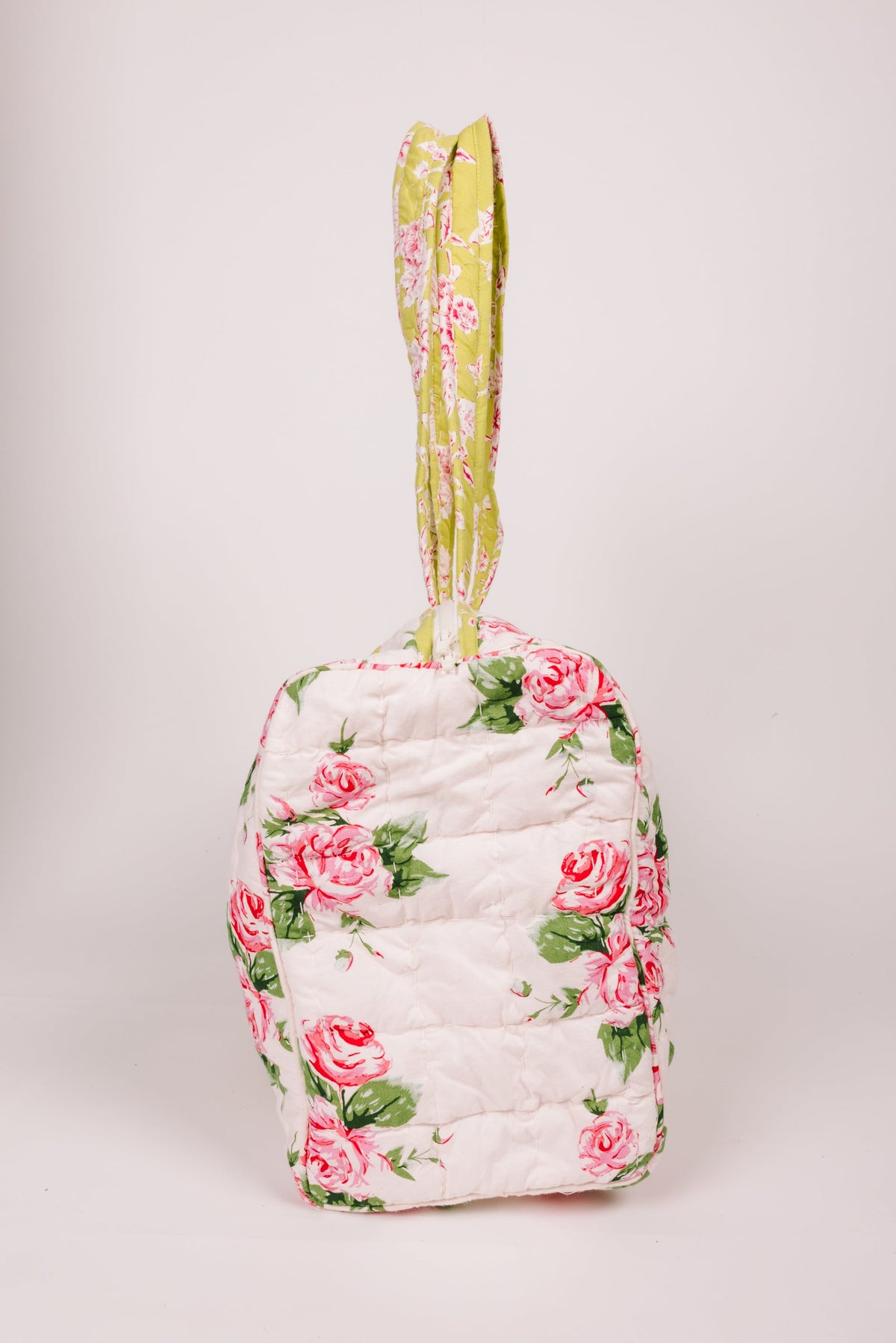 Floral quilted duffle bag standing upright with pink roses and yellow-green handle
