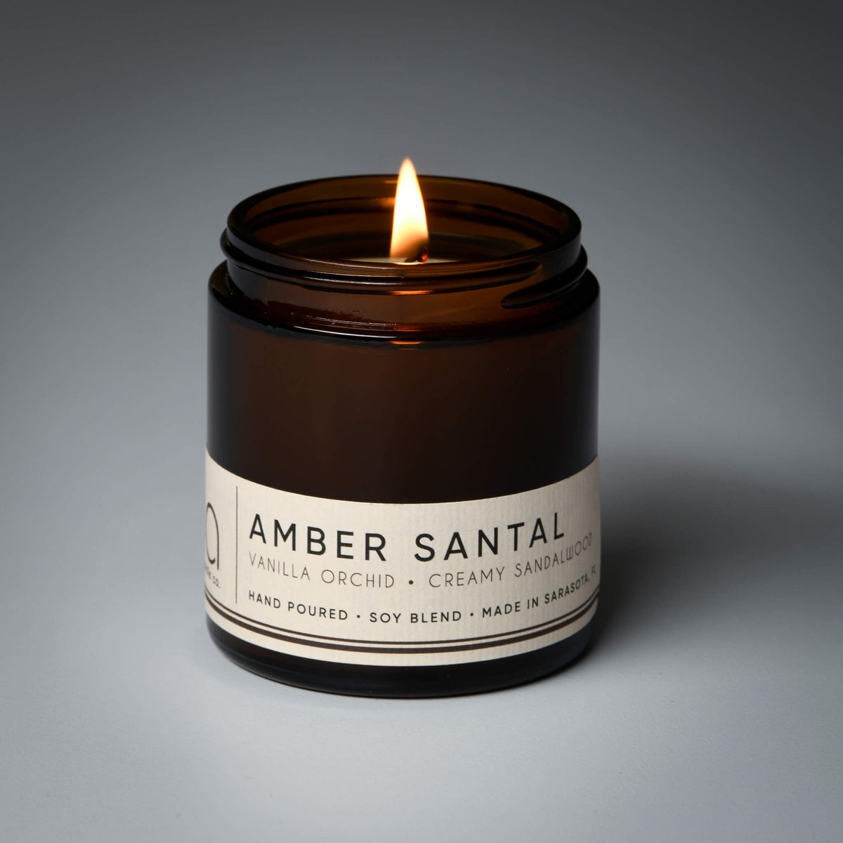Amber Santal soy blend candle burning in an open amber glass jar with a cream label.