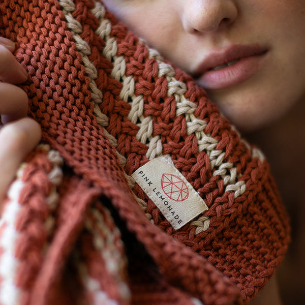 Rust knit throw blanket close-up with cream stripes and woven brand tag