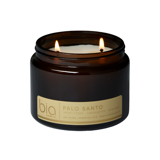 Dark glass soy candle jar with two flames and “Palo Santo” label on front
