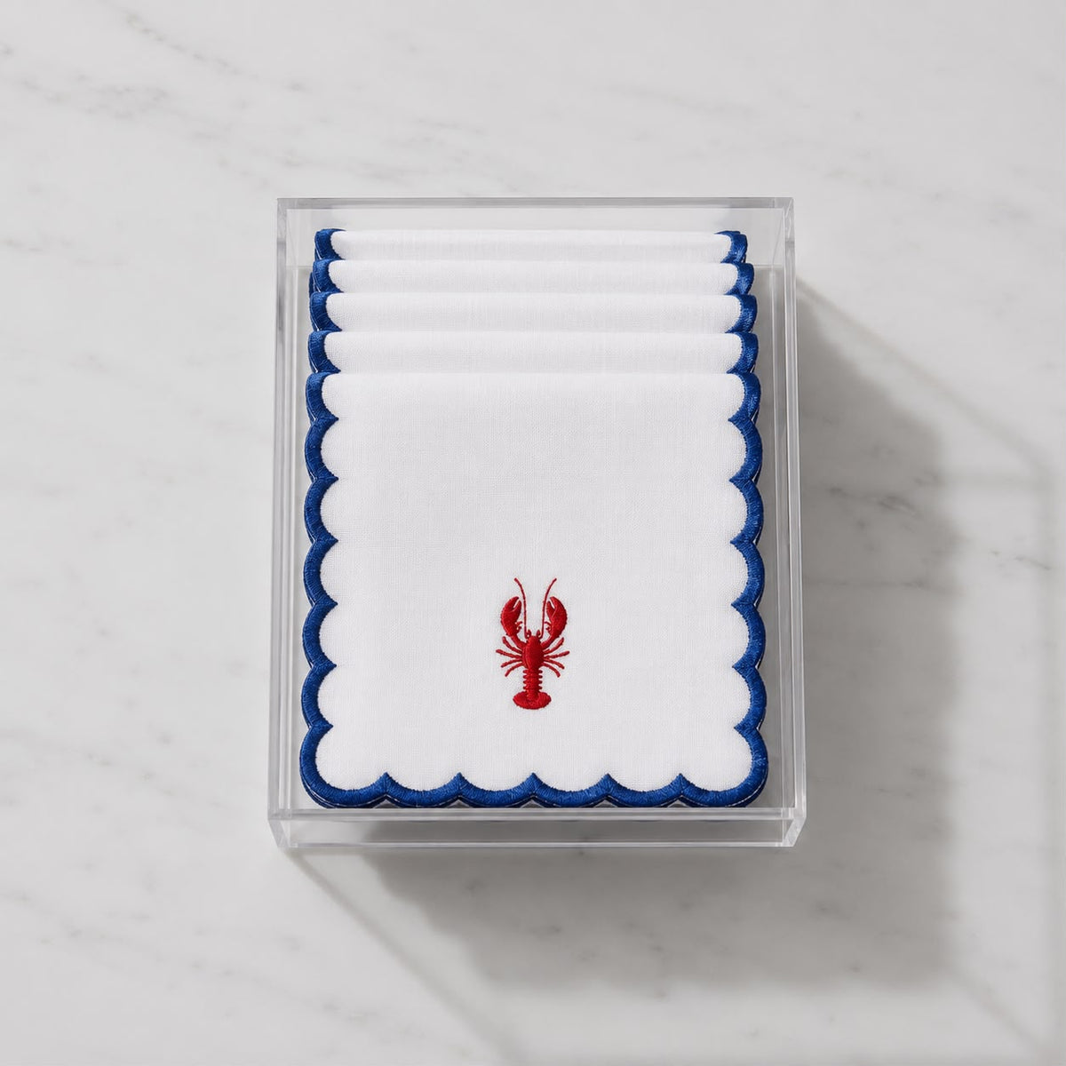 Stacked nautical cocktail napkins in clear holder, white with navy scalloped trim and red lobster