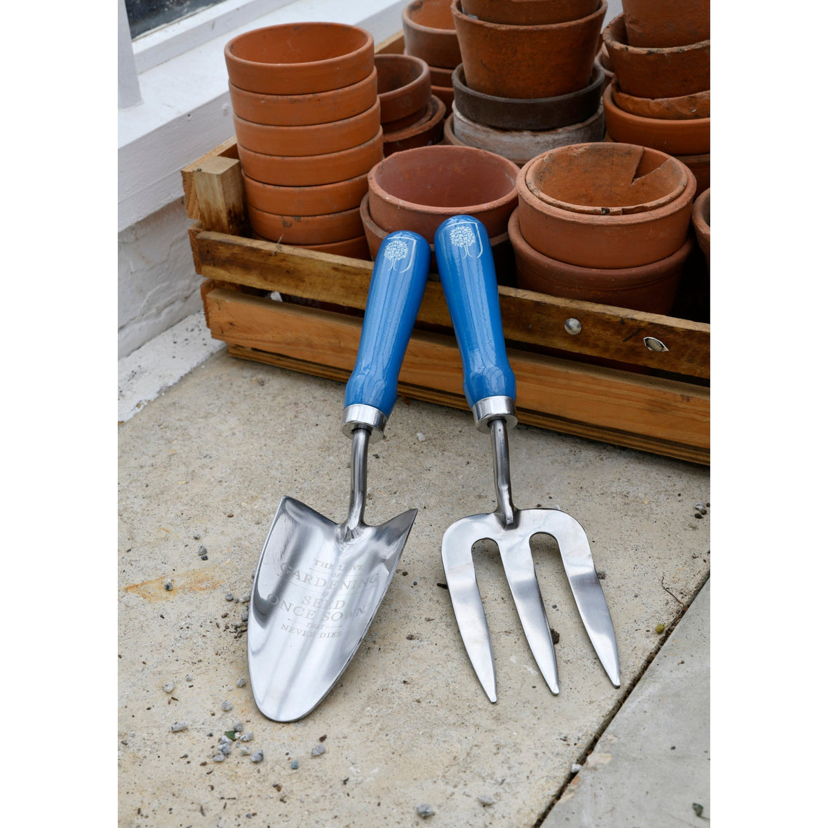 Blue-handled trowel and fork on patio floor near stacked terracotta pots