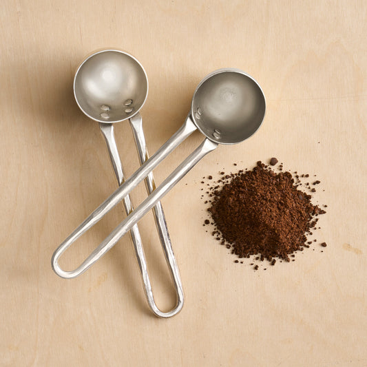 Pewter coffee scoop set of 2 with long handles, one scoop spilling dark coffee grounds
