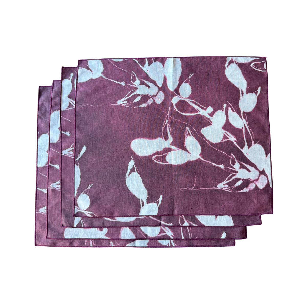 Stack of rectangular aubergine placemats with light blue floral print and stitched edges.