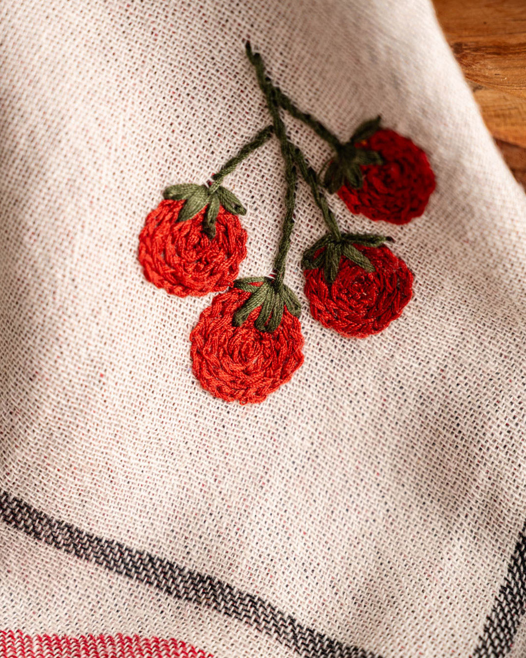 Beige kitchen towel with detailed red tomato embroidery and subtle gray check edging