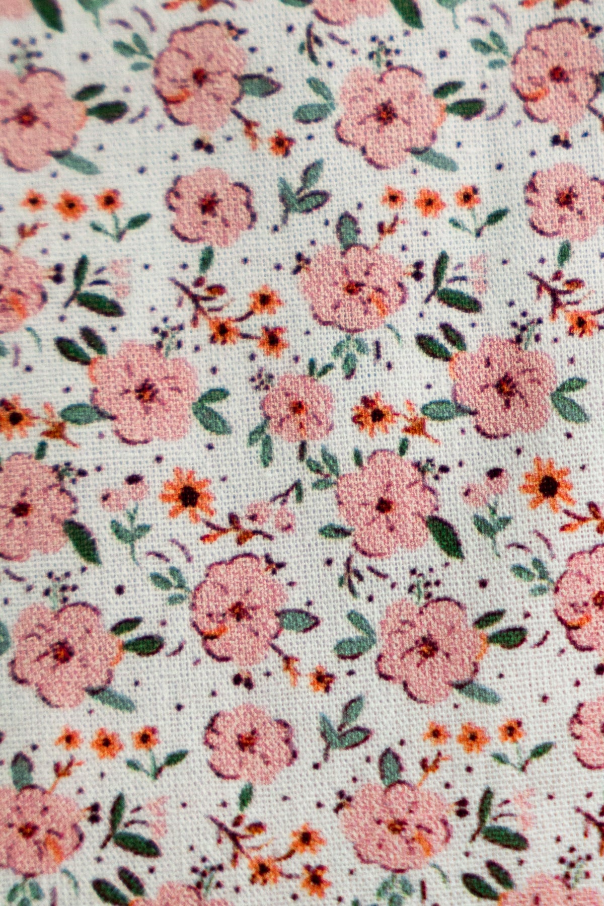 Close-up of peach floral fabric with small flowers and green leaf pattern