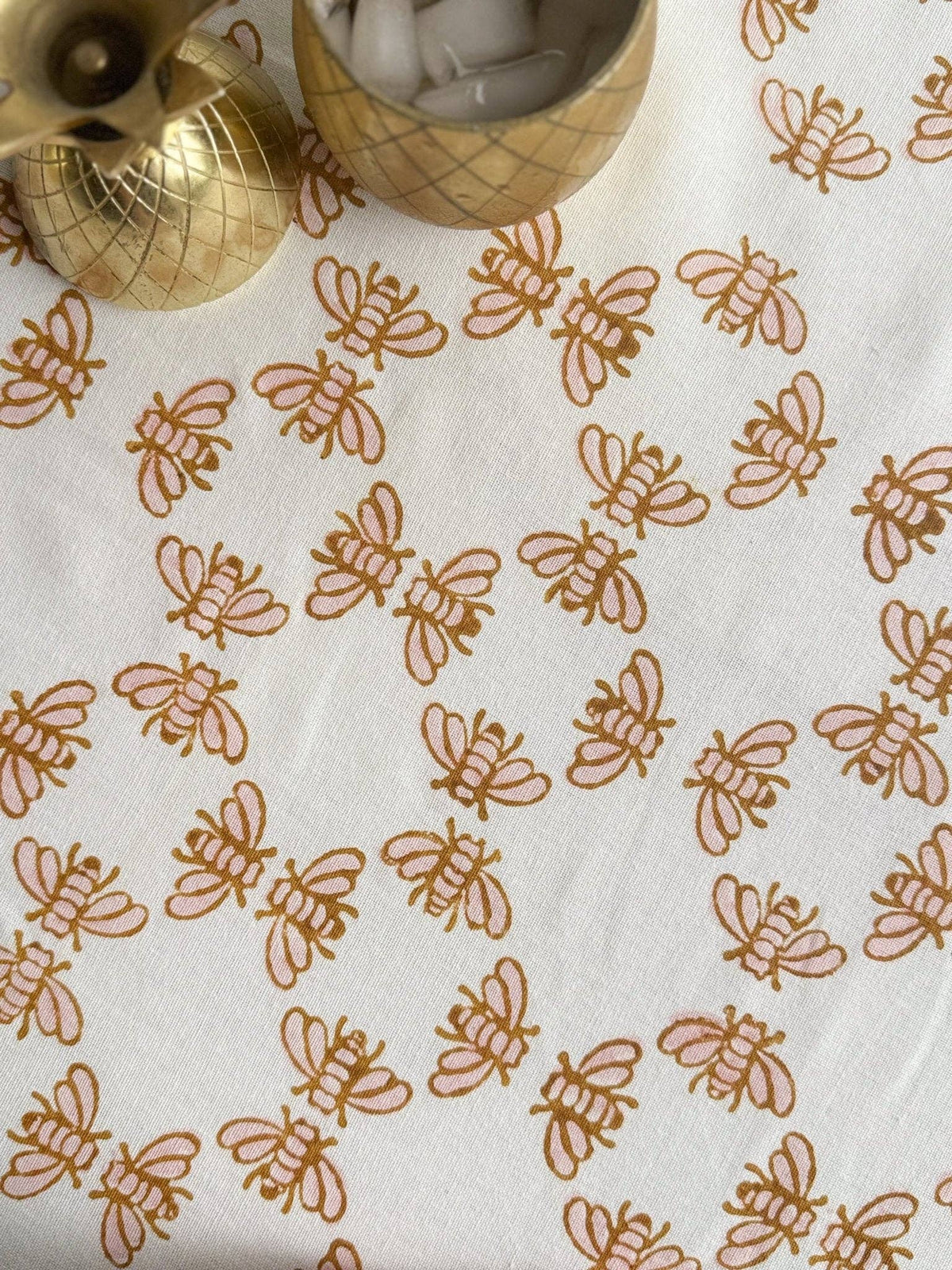 White table throw with repeating honeybee and vine motifs in rose and mustard