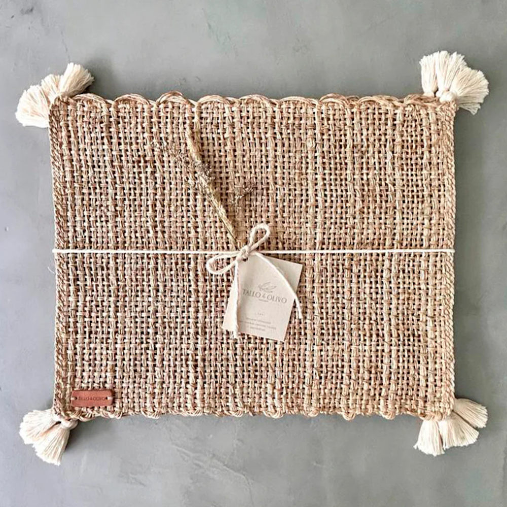 Tan woven rectangular placemat with corner tassels and hanging product tag