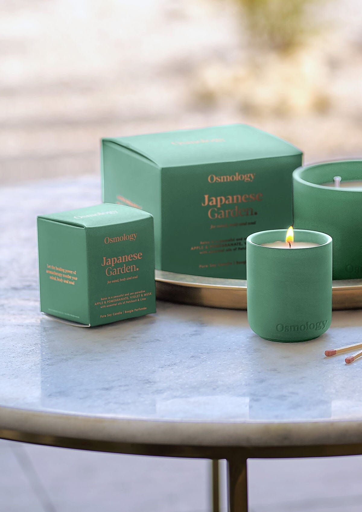 Lit mint green triple-wick candle with three flames and Japanese Garden gift boxes