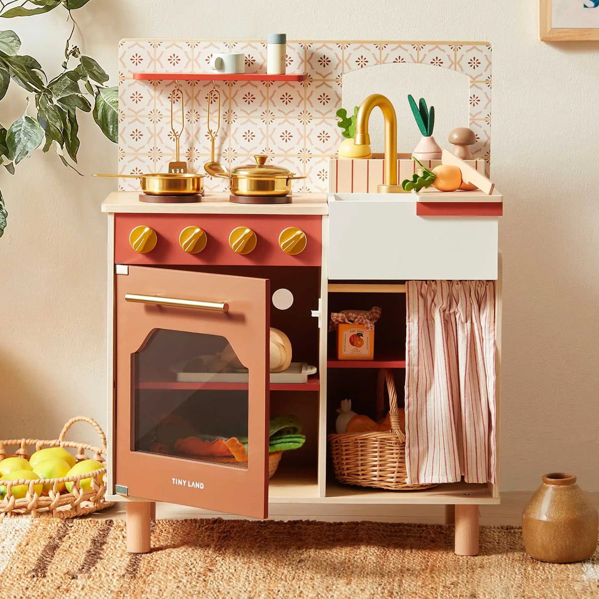 Tiny Land wooden play kitchen with rust-colored oven, white sink, faucet, and striped storage curtain