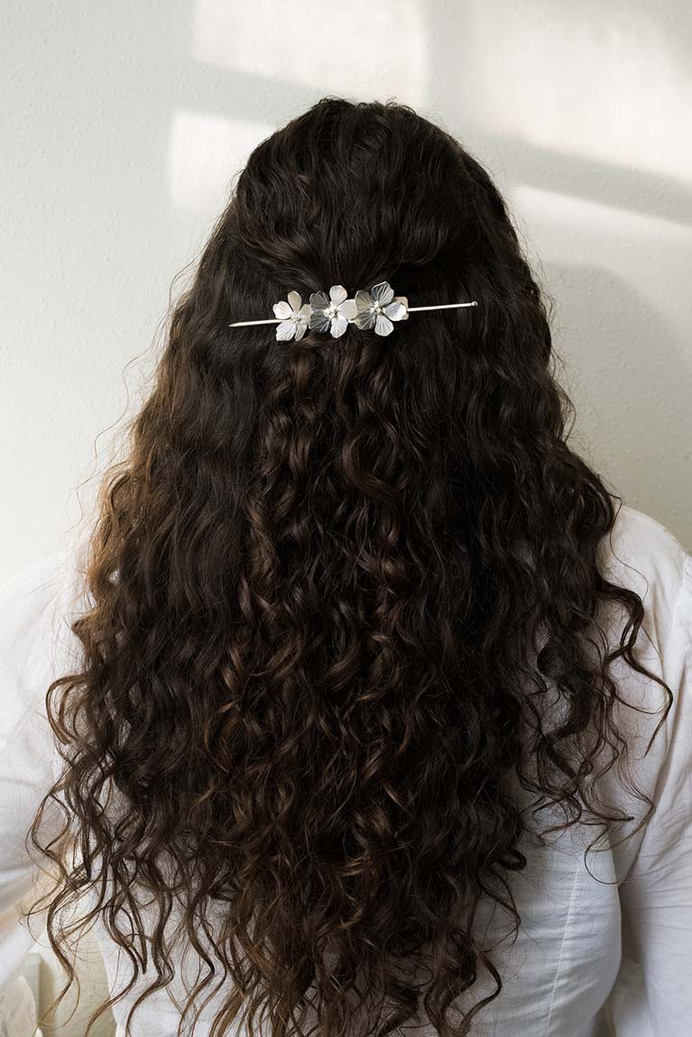 Silver flower hair pin across the back of dark, wavy hair with three blossoms