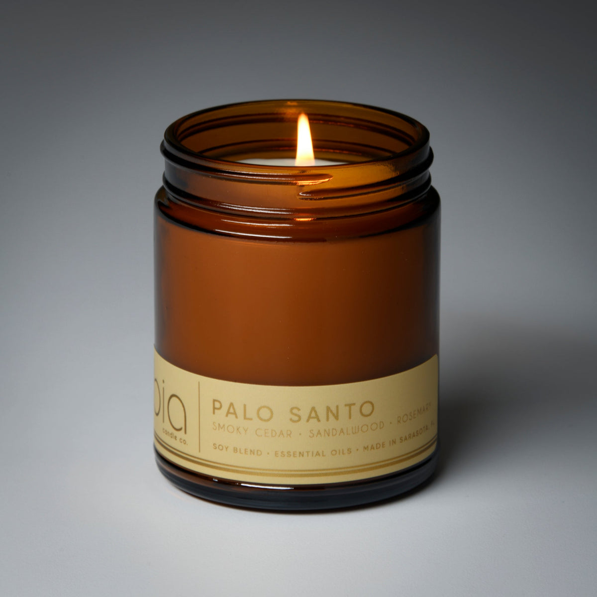 Amber glass soy candle jar with burning flame and “Palo Santo” label on front