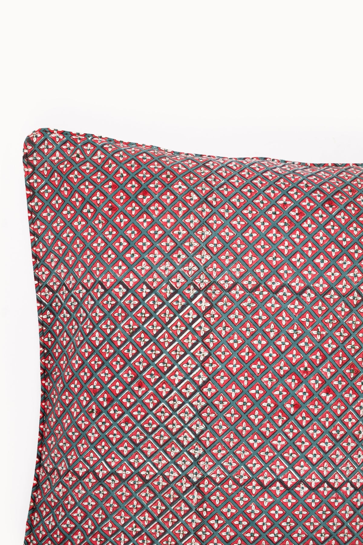 Close-up of crimson diamond-pattern pillow cover with dark piped border