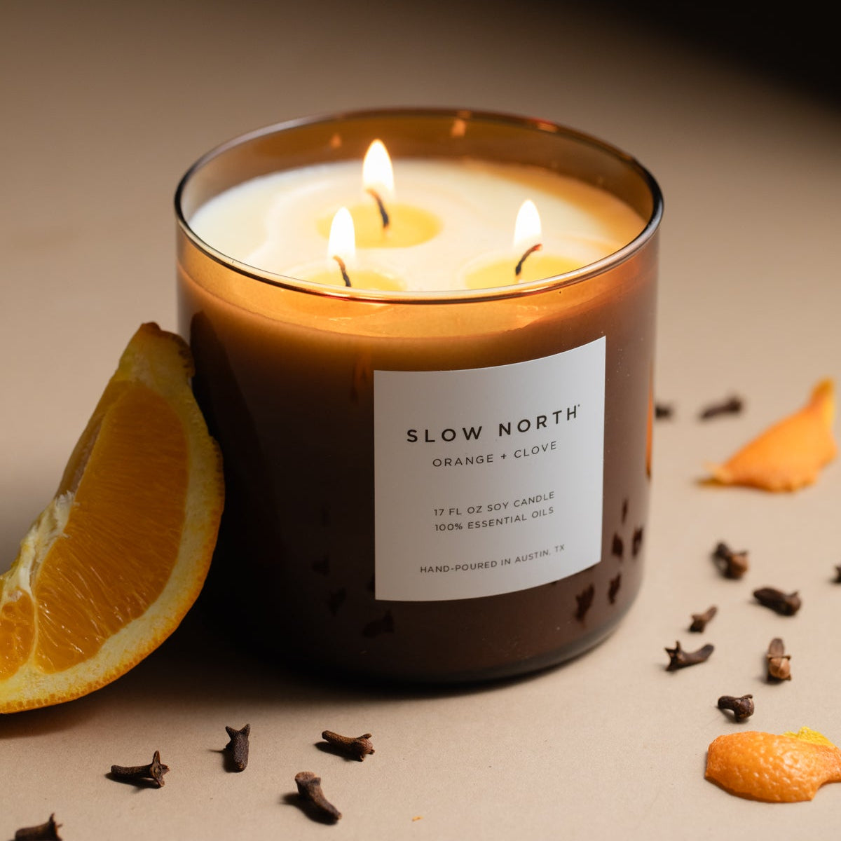 Slow North 3-wick candle with orange-clove label, amber wax, and three burning wicks