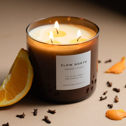 Slow North 3-wick candle with orange-clove label, amber wax, and three burning wicks