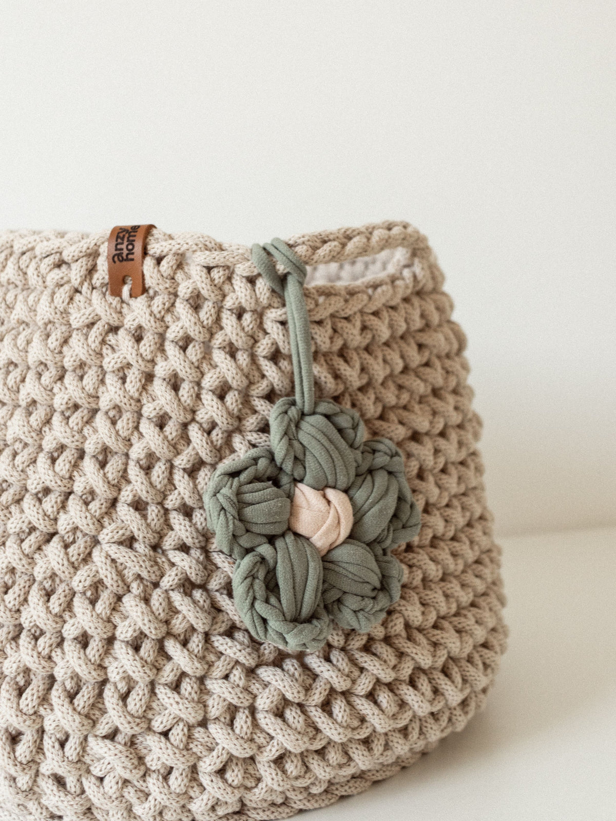 Close-up of cream crochet storage basket with muted green braided flower applique