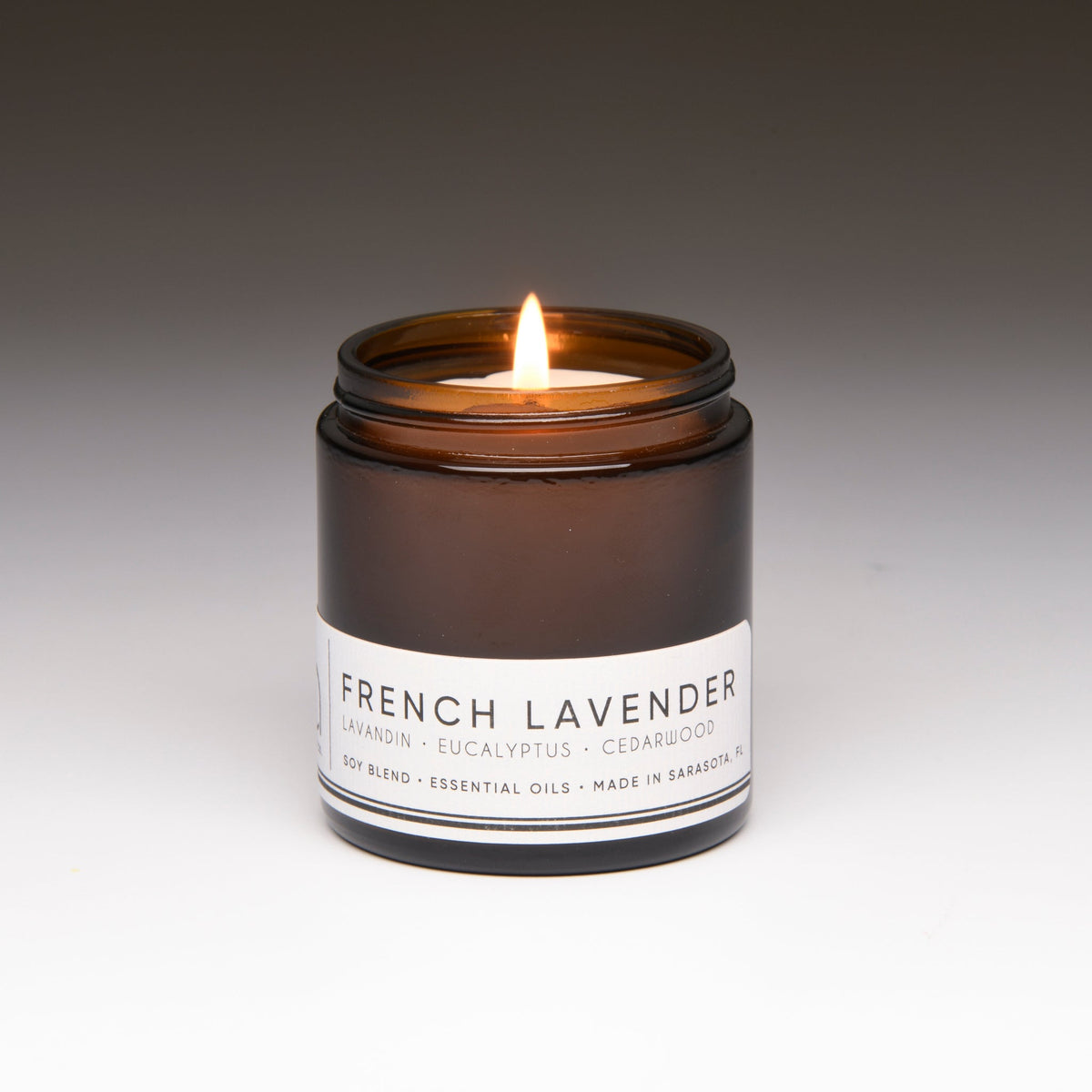 Amber soy candle jar with lit wick, centered front label visible