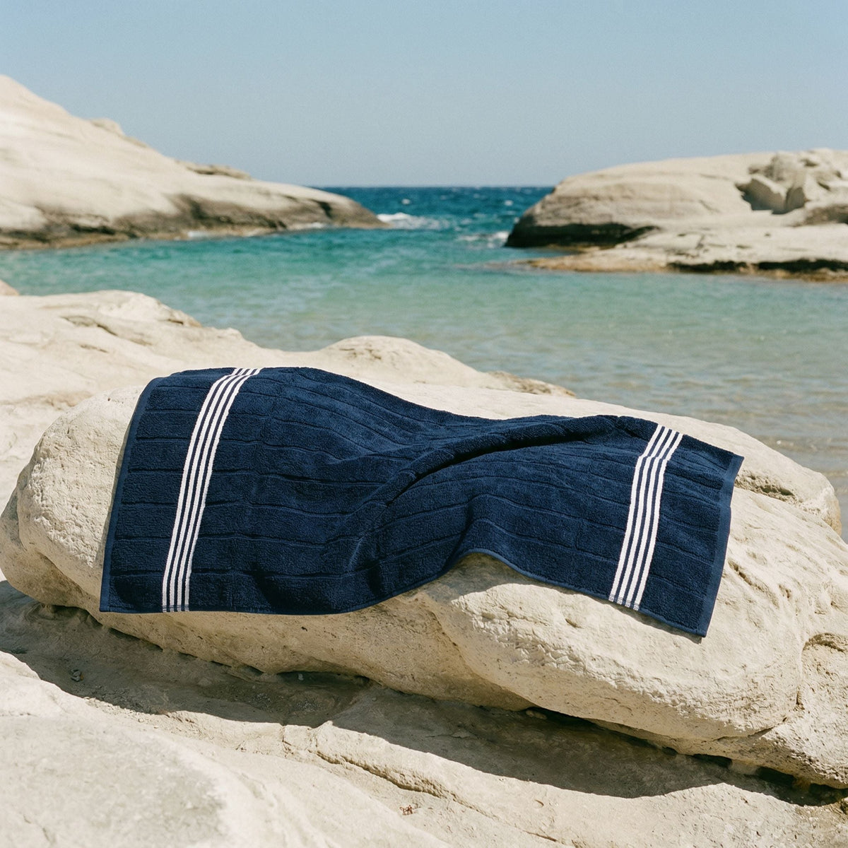 Navy cotton towel with white stripe bands draped over pale rocks