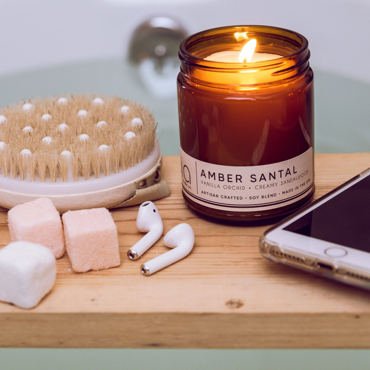Amber glass candle jar burning next to a wooden brush and small cream-colored wax shapes.