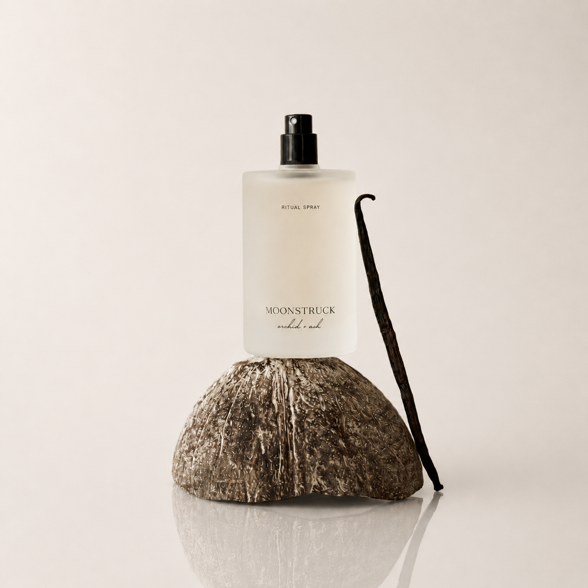 Ritual spray bottle with black pump and dark vanilla bean on white surface