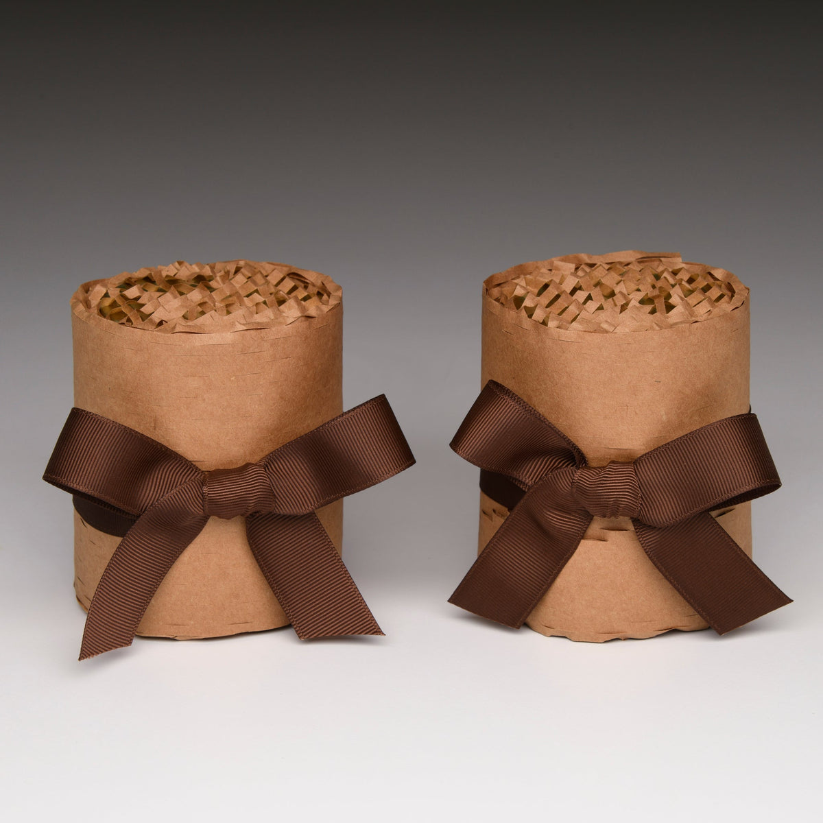 Two kraft paper candle gift boxes with brown ribbon bows, stacked side by side