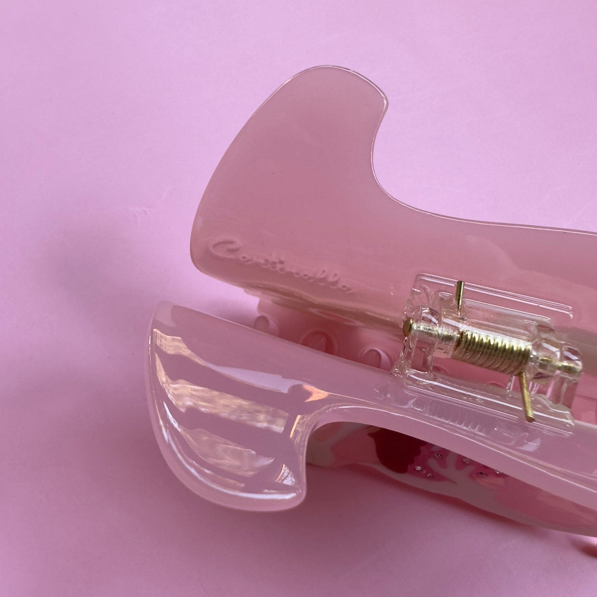 Pink translucent hair claw close-up showing metal spring hinge and teeth