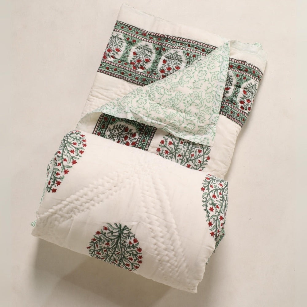 Folded reversible quilt with white base, mint vine print, and red tree motifs