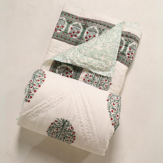 Folded reversible quilt with white base, mint vine print, and red tree motifs