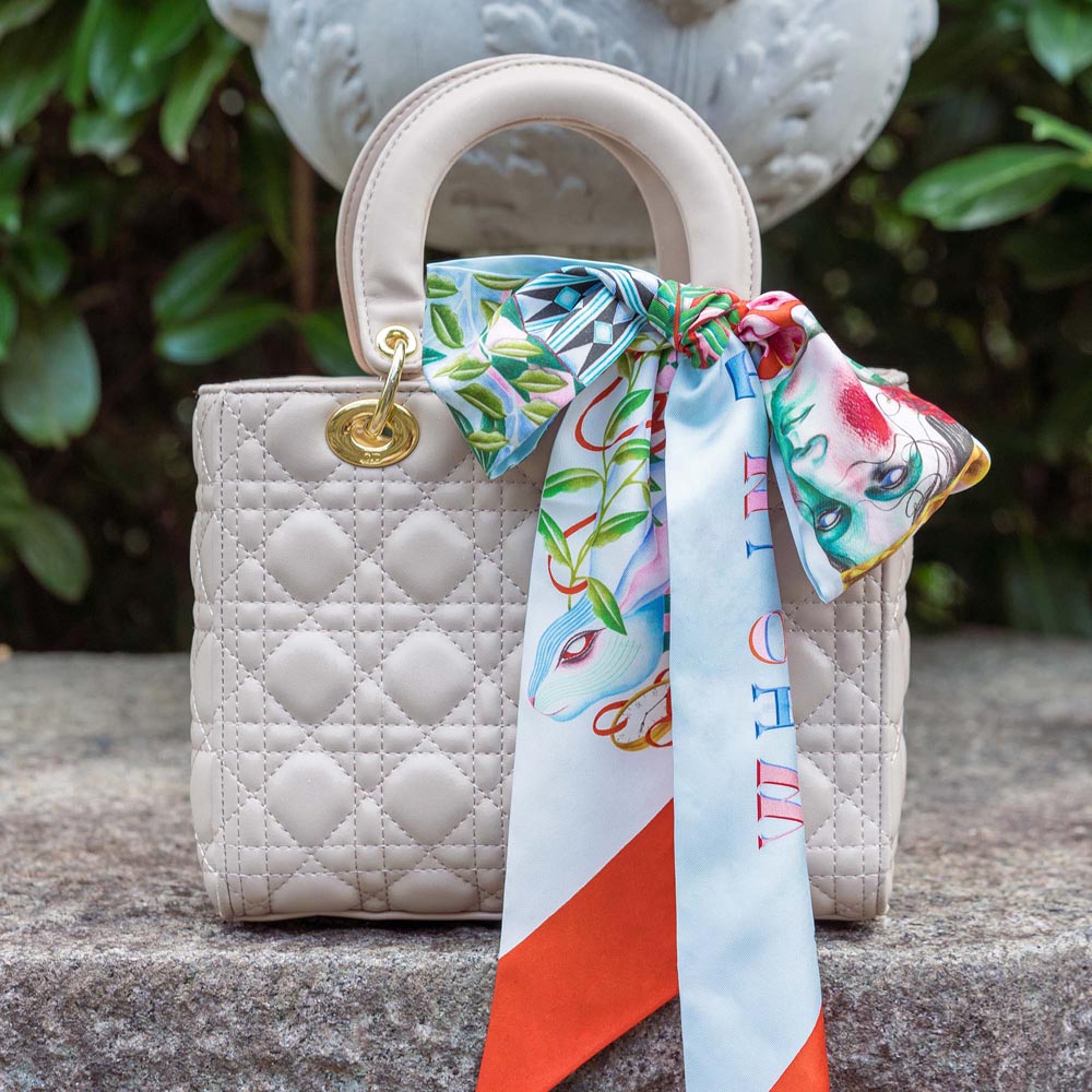 Silk twilly scarf tied to a white quilted bag, light blue with birds and red tips